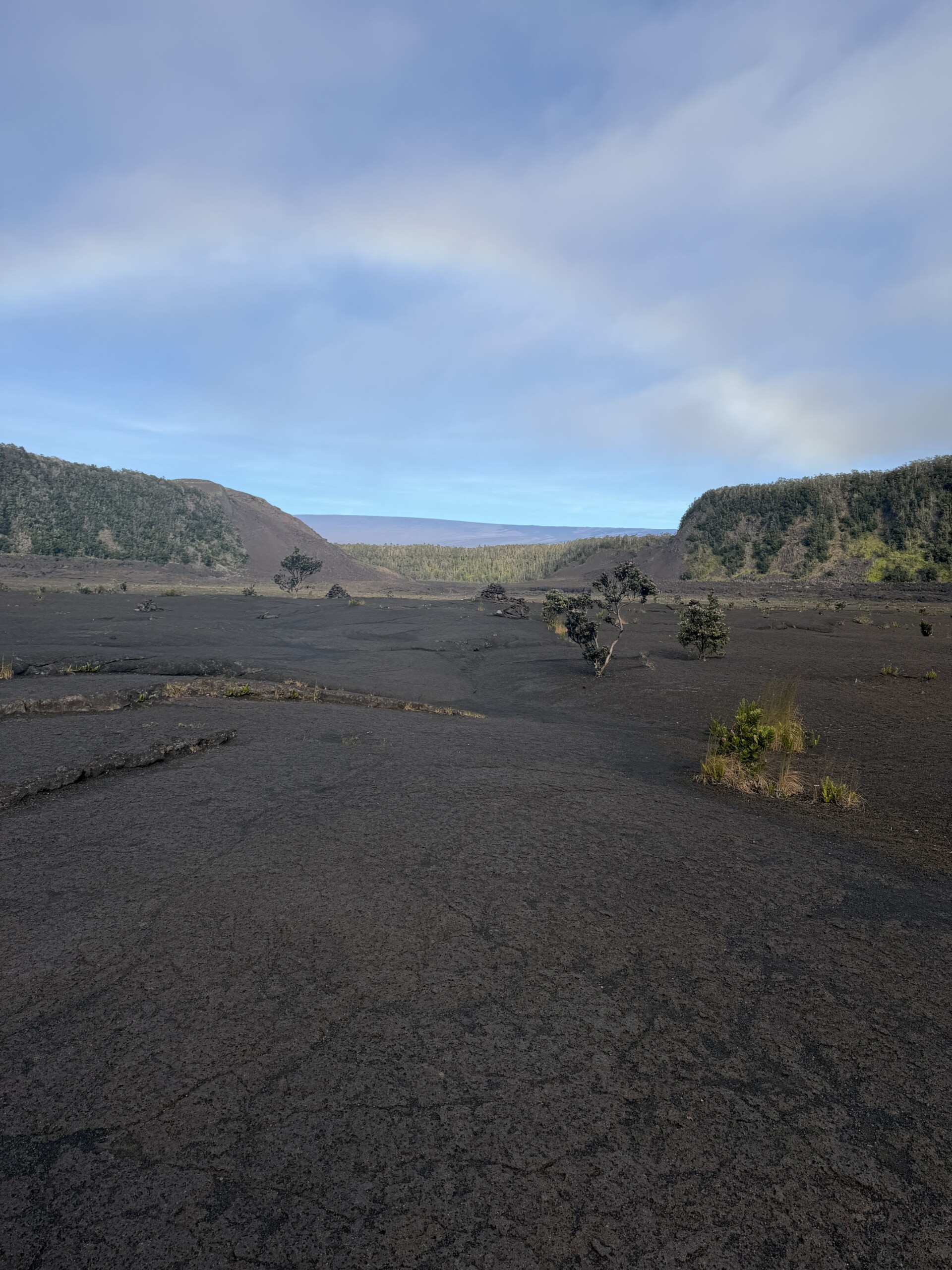 Trail crossing a dark volcanic crater floor beneath cloudy skies