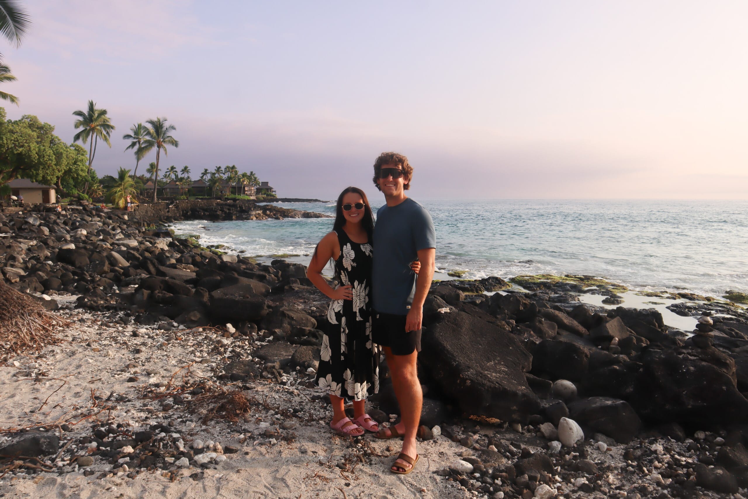 Brendon and Kaylee standing on a rocky Big Island shoreline at sunset