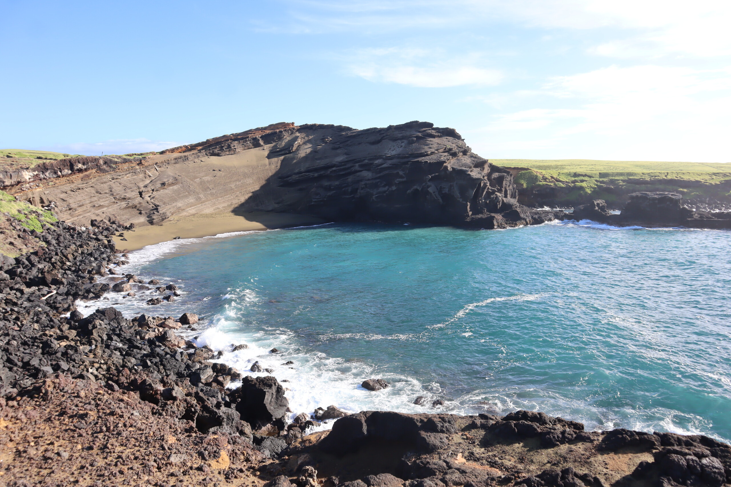Green sand beach in a curved coastal cove with turquoise water