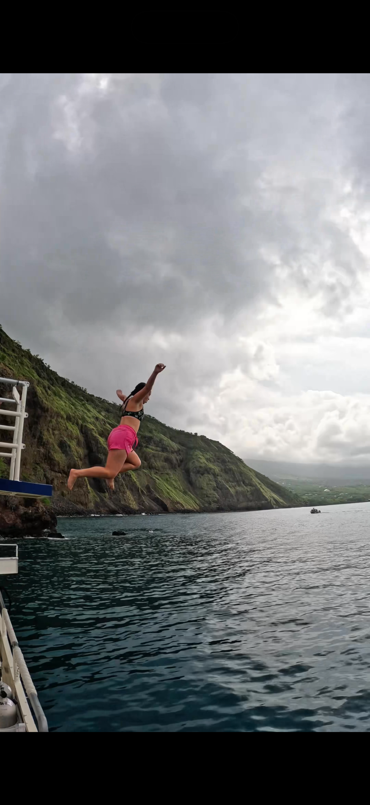A person jumping from a boat into the ocean below green coastal cliffs